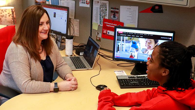 Student talking at desk with staff